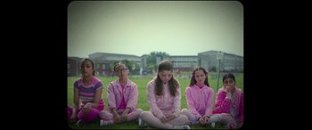 Movie still from “Scrapper” (2023), directed by Charlotte Regan – A group of young girls sitting on the grass; Wide shot, Low angle