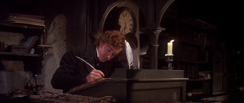 Movie still from “Scrooge” (1970), directed by Ronald Neame – A young man is writing on a piece of paper; Medium shot, Low angle