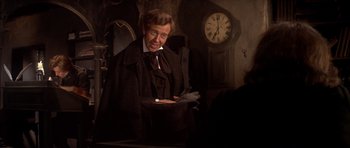 Movie still from “Scrooge” (1970), directed by Ronald Neame – An old man in a suit and tie holding a hat; Medium shot, Over the shoulder angle