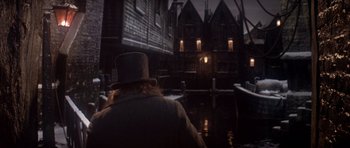 Movie still from “Scrooge” (1970), directed by Ronald Neame – A man wearing a top hat and a long coat standing in front of a building; Wide shot, High angle