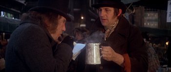 Movie still from “Scrooge” (1970), directed by Ronald Neame – Two men are holding a steaming cup of hot chocolate; Medium shot, Over the shoulder angle