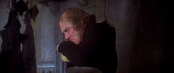 Movie still from “Scrooge” (1970), directed by Ronald Neame – A man sitting in a chair with his head resting on his arms; Medium shot, Low angle