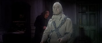 Movie still from “Scrooge” (1970), directed by Ronald Neame – A man standing next to a statue of a man chained to a wall; Medium shot, Low angle