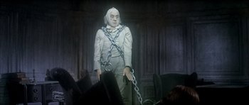 Movie still from “Scrooge” (1970), directed by Ronald Neame – A man chained to a chair in a dark room; Medium shot, High angle