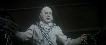 Movie still from “Scrooge” (1970), directed by Ronald Neame – A statue of a man with a chain around his neck; Medium shot, Low angle