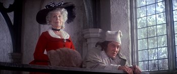Movie still from “Scrooge” (1970), directed by Ronald Neame – A man and a woman sitting next to each other in front of a wall; Medium shot, Low angle