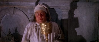 Movie still from “Scrooge” (1970), directed by Ronald Neame – A man wearing a white hat and holding a gold goblet; Medium shot, Overhead angle