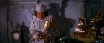 Movie still from “Scrooge” (1970), directed by Ronald Neame – A man holding a goblet while wearing a white hat; Medium shot, Low angle