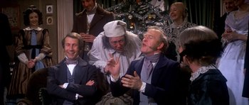 Movie still from “Scrooge” (1970), directed by Ronald Neame – A group of people sitting in front of a christmas tree; Medium shot, Over the shoulder angle