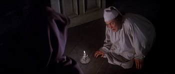 Movie still from “Scrooge” (1970), directed by Ronald Neame – An old woman sitting on the floor next to a lit candle; Medium shot, High angle