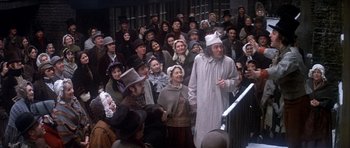 Movie still from “Scrooge” (1970), directed by Ronald Neame – A group of people standing in front of an audience; Wide shot, High angle