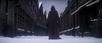 Movie still from “Scrooge” (1970), directed by Ronald Neame – A person in a hooded cloak standing in the middle of a snowy street; Wide shot, Low angle