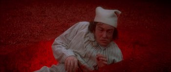 Movie still from “Scrooge” (1970), directed by Ronald Neame – A man wearing a white hat and a striped shirt is laying on the ground; Medium shot, High angle
