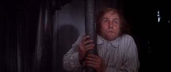 Movie still from “Scrooge” (1970), directed by Ronald Neame – A man holding onto a metal pole in a dark room; Medium shot, Low angle
