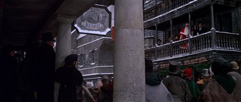 Movie still from “Scrooge” (1970), directed by Ronald Neame – A group of people standing around a building; Extreme Wide shot, High angle