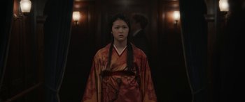 Movie still from “1899” (2022), created by Jantje Friese – A woman in a red and orange kimono standing in front of a door; Medium shot, Low angle