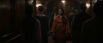 Movie still from “1899” (2022), created by Jantje Friese – A woman in a red and orange dress standing in front of other people; Medium shot, Over the shoulder angle