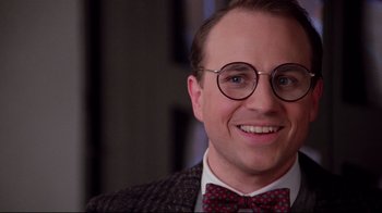 Movie still from “Scrooged” (1988), directed by Richard Donner – A person wearing glasses and a bow tie; Close Up shot, Over the shoulder angle