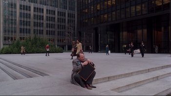 Movie still from “Scrooged” (1988), directed by Richard Donner – A man sitting on the ground holding a briefcase; Wide shot, High angle