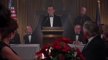 Movie still from “Scrooged” (1988), directed by Richard Donner – A man in a tuxedo standing at a podium in front of a group of people; Medium shot, Low angle