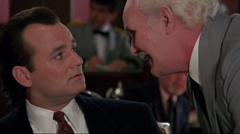 Movie still from “Scrooged” (1988), directed by Richard Donner – Two men in business suits talking to each other; Close Up shot, Over the shoulder angle