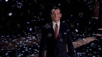 Movie still from “Scrooged” (1988), directed by Richard Donner – A man wearing a suit and tie standing in front of a wall of confetti; Medium shot, Low angle