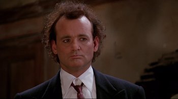 Movie still from “Scrooged” (1988), directed by Richard Donner – A man in a suit and tie with curly hair looking at the camera; Close Up shot, Low angle