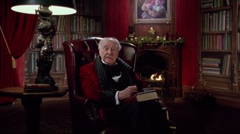 Movie still from “Scrooged” (1988), directed by Richard Donner – An older man sitting in a chair holding a book; Medium shot, Low angle