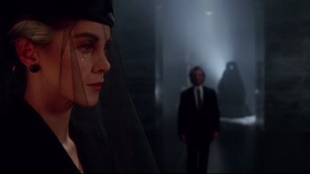 A woman with a veil on her head looking at a man in a suit and tie