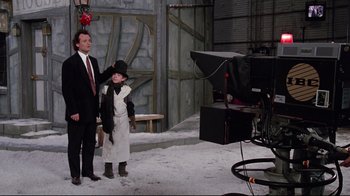 Movie still from “Scrooged” (1988), directed by Richard Donner – A man standing next to a young boy in a suit; Wide shot, Over the shoulder angle