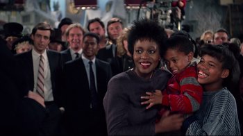 Movie still from “Scrooged” (1988), directed by Richard Donner – A woman holding a child in front of a group of people; Close Up shot, Over the shoulder angle