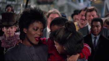 Movie still from “Scrooged” (1988), directed by Richard Donner – A group of people gathered around a woman with her arms around a young girl; Close Up shot, Over the shoulder angle