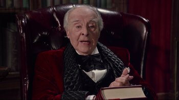 Movie still from “Scrooged” (1988), directed by Richard Donner – An old man sitting in a red chair wearing a bow tie; Medium shot, Low angle