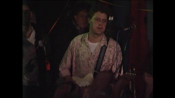Movie still from “Searching for Sugar Man” (2012), directed by Malik Bendjelloul – A man holding a guitar in front of a crowd; Medium shot, Low angle