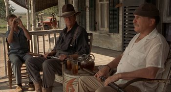 Movie still from “Secondhand Lions” (2003), directed by Tim McCanlies – A man sitting on a barrel on a porch; Medium shot, Low angle