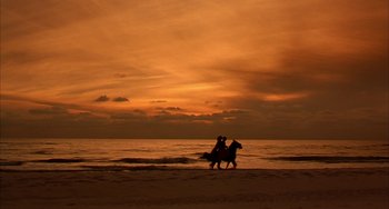 Movie still from “Secondhand Lions” (2003), directed by Tim McCanlies – Two people ride horses on the beach at sunset; Extreme Wide shot, Low angle