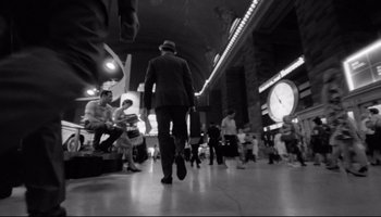 Movie still from “Seconds” (1966), directed by John Frankenheimer – A black and white photo of a man in a suit and hat walking through a train station; Wide shot, Low angle