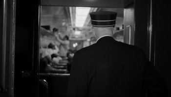 Movie still from “Seconds” (1966), directed by John Frankenheimer – A black and white photo of a man in a train car; Medium shot, Over the shoulder angle