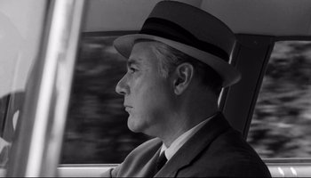 Movie still from “Seconds” (1966), directed by John Frankenheimer – An older man wearing a suit and a hat driving a car; Close Up shot, Over the shoulder angle