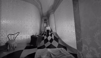 Movie still from “Seconds” (1966), directed by John Frankenheimer – A man standing in front of a checkerboard quilt in a room; Wide shot, High angle