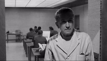 Movie still from “Seconds” (1966), directed by John Frankenheimer – Black and white photograph of a man in front of a class room; Medium shot, Over the shoulder angle