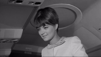 Movie still from “Seconds” (1966), directed by John Frankenheimer – A woman in a white dress is standing in an airplane; Close Up shot, Low angle