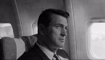 Movie still from “Seconds” (1966), directed by John Frankenheimer – Black and white photograph of a man in a suit and tie on an airplane; Close Up shot, Low angle
