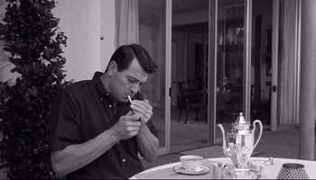 Movie still from “Seconds” (1966), directed by John Frankenheimer – A black and white photo of a man smoking a cigarette at a table; Medium shot, Low angle