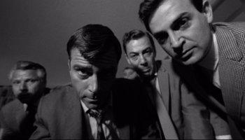 Movie still from “Seconds” (1966), directed by John Frankenheimer – A black - and - white photo of three men in suits; Medium shot, Low angle