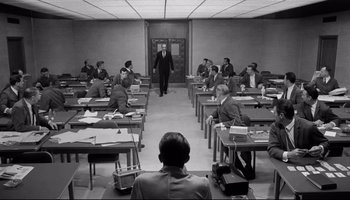 Movie still from “Seconds” (1966), directed by John Frankenheimer – A group of men sitting at desks in a room; Wide shot, High angle