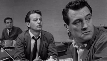 Movie still from “Seconds” (1966), directed by John Frankenheimer – A man sitting next to another man in front of a wall; Close Up shot, Low angle