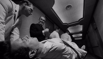 Movie still from “Seconds” (1966), directed by John Frankenheimer – A group of men standing next to each other in a room; Medium shot, Low angle