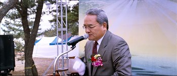 Movie still from “Secret Sunshine” (2007), directed by Lee Chang-dong – A man in a suit and tie speaking into a microphone; Medium shot, Low angle