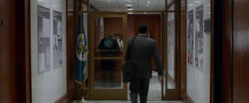 Movie still from “Secret in Their Eyes” (2015), directed by Billy Ray – A man in a business suit walks through an entrance to a building; Wide shot, Over the shoulder angle